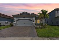 Beautiful home with lush lawn, stone accents, brick driveway and a two-car garage at sunset at 31046 Lindentree Dr, Wesley Chapel, FL 33543