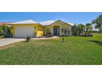 Charming yellow single-story home featuring a well-manicured lawn and beautifully landscaped flower beds at 12 Medalist Ter, Rotonda West, FL 33947