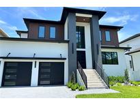 Contemporary home features a black two-car garage, and landscaped yard with modern staircase leading to the front door at 5017 W Dickens Ave, Tampa, FL 33629