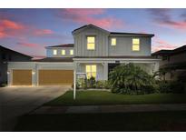 Charming two-story home with a well-manicured lawn, attached garage, and inviting curb appeal at dusk at 7811 Roma Dune Dr, Wesley Chapel, FL 33545