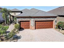 A large, stone-accented, 2-car garage with brick-paved driveway and mature landscaping at 11424 Drifting Leaf Dr, Riverview, FL 33579