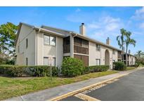 A charming condo building with tan stucco, brown balconies, well-maintained landscaping, and a glimpse of a palm tree at 2087 Hunters Glen Dr # 126, Dunedin, FL 34698