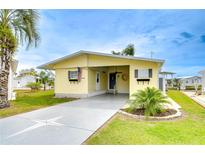 Charming yellow home featuring a covered carport, well-manicured lawn, and tropical landscaping at 35246 Tiffani Ct, Zephyrhills, FL 33541