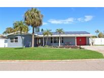 Charming single-story home with well-manicured lawn, palm trees, and solar panels against a clear blue sky at 4301 50Th S Ter, St Petersburg, FL 33711