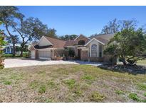 Charming single-story home featuring a three-car garage, brick accents, lush trees and meticulous landscaping at 18739 Bascomb Ln, Hudson, FL 34667