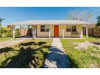 Charming single-story home featuring a covered porch with a swing, bright orange door, and a well-manicured lawn at 14031 E Parsley Dr, Madeira Beach, FL 33708