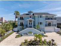 Stunning three-story blue home featuring a grand staircase, multiple balconies, lush landscaping, and brick driveway at 289 8Th N Ave, Tierra Verde, FL 33715
