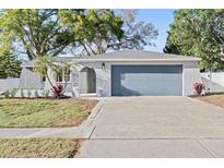 Charming single-story home featuring a blue garage door, arched entryway, and fresh landscaping at 1972 Sourwood Blvd, Dunedin, FL 34698