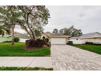 Charming home featuring a brick paver driveway leading to an attached garage and lush landscaping at 1526 River Ct, Tarpon Springs, FL 34689