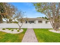Charming single-story home with a well-manicured lawn, a white picket fence, and a brick walkway at 292 42Nd Ave, St Pete Beach, FL 33706