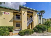 A charming yellow condo building with well-maintained landscaping, white stairs, and clearly marked unit numbers at 6125 113Th St # 515, Seminole, FL 33772