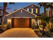 Two-story home showcasing a well-manicured front yard with lush landscaping, palm trees, and a large two-car garage at dusk at 4522 Tramanto Ln, Wesley Chapel, FL 33543