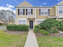 Two-story townhome featuring manicured landscaping, black shutters, tan stucco, and a welcoming walkway to the front door at 1256 Redondo Way, Wesley Chapel, FL 33543