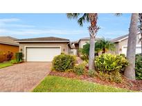 Charming single-story home with lush tropical landscaping, a paved driveway, and a two-car garage at 15644 Aurora Lake Cir, Wimauma, FL 33598