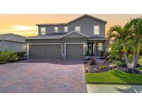 Two-story home featuring a two-car garage, brick driveway, manicured landscaping, and a palm tree in the front yard at 11605 Cleyera Ct, Riverview, FL 33579