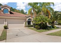Charming home featuring a tile roof, two-car garage, and beautiful tropical landscaping with mature palm trees at 3798 Darston St, Palm Harbor, FL 34685