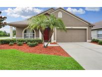Inviting home featuring a two-car garage, tidy landscaping and a red front door at 30142 Sotogrande Loop, Wesley Chapel, FL 33543