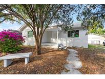 Charming one-story home with a white exterior, stone bench, lush landscaping, and inviting walkway at 2910 N 17Th St, Tampa, FL 33605