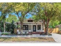 Charming bungalow with a white exterior, front porch, and mature trees in a lush, landscaped front yard at 710 E Plymouth St, Tampa, FL 33603