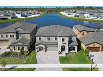 Stunning two-story home featuring stone accents, a paver driveway, manicured lawn, and a serene lake view at 12851 Tortoise Shell Pl, Riverview, FL 33579