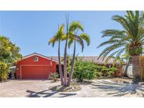 Charming one-story home with a red exterior, tile roof, and lush tropical landscaping at 351 S Julia Cir, St Pete Beach, FL 33706