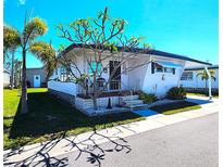 Inviting home with white siding, a quaint front porch, well-kept lawn and mature landscaping at 34111 Alamanda N Dr, Pinellas Park, FL 33781