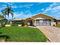 Charming home featuring a lush lawn, mature landscaping, and a brick driveway leading to an attached two-car garage at 8621 Bridgewater Dr, New Port Richey, FL 34655