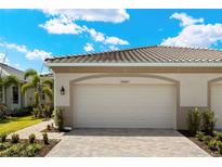 View of a two-car garage with a brick paver driveway and manicured landscaping in front of the property at 20405 Symphony Pl, Venice, FL 34293
