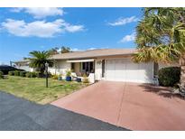 Charming single-story home featuring a red driveway, lush lawn, and mature palm trees under a clear blue sky at 312 Fairside Ct # 12, Sun City Center, FL 33573