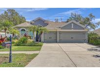 Charming home featuring a well-manicured lawn, lush landscaping, and an attached three-car garage at 10810 Moss Island Dr, Riverview, FL 33569