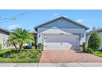Charming single-Gathering home featuring a well-manicured lawn, lovely palm tree, and brick driveway leading to a two-car garage at 19437 Ship Wheel Way, Land O Lakes, FL 34638