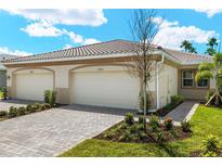 Home exterior displaying a two-car garage, a paver driveway, and landscaping in front of the home under a cloudy blue sky at 20411 Symphony Pl, Venice, FL 34293