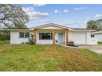 Charming single-story home featuring a manicured lawn and a welcoming blue front door, complemented by wood support beams at 7310 Donna Dr, New Port Richey, FL 34652