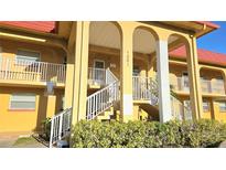 Exterior shot of building with yellow facade, white stair railings, and beautiful landscaping at 1301 S Hercules Ave # 3, Clearwater, FL 33764