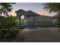 Charming single-Gathering home with a three-car garage and a well-manicured lawn at dusk at 1210 Paradise Lake Dr, Tarpon Springs, FL 34689