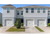 Charming two-story townhome featuring a gray exterior, a well-manicured lawn, and individual car garages at 12309 Grizzly Ln, New Port Richey, FL 34654