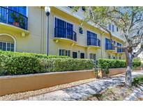 Charming yellow townhome featuring black metal balconies and lush green landscaping along the front walkway at 133 S Sherrill St # 133, Tampa, FL 33609