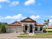 Charming single-story home featuring a red tile roof, arched entryway, and a two-car garage set against a sunny sky at 3635 80Th E Dr, Sarasota, FL 34243