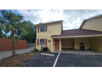 Two-story condo with yellow stucco, brown trim, and covered parking on cracked blacktop at 7502 Bolanos Ct, Tampa, FL 33615