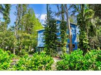 Charming blue two-story home surrounded by lush greenery and mature trees with hanging moss at 18716 Lake Commiston Dr, Lutz, FL 33549