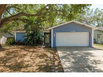 Charming home featuring a lush, landscaped yard with mature trees and a two-car garage at 1721 Sutton Pl, Dunedin, FL 34698