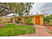 Charming yellow home with an orange door, lush green lawn, and mature landscaping at 401 Dorchester Pl # 69, Sun City Center, FL 33573