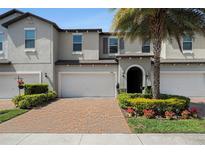 Charming two-story townhome features a brick driveway, attached garage, and beautifully landscaped front yard with a palm tree at 10106 Corso Milano Dr, Tampa, FL 33625