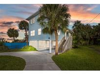 Inviting coastal home with light blue siding, a lush green lawn, and swaying palm trees at 3457 Cyclone Dr, Weeki Wachee, FL 34607
