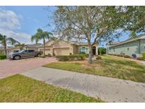 Charming tan home featuring lush landscaping, a brick driveway, and a two-car garage at 807 Chipper Dr, Sun City Center, FL 33573