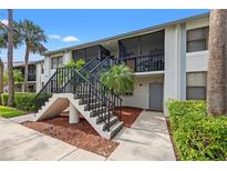 Condo building with white exterior, stairs, and beautiful landscaping with palms leading to a screened in porch at 1986 Pelican Landing Blvd # 1514, Clearwater, FL 33762