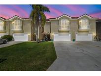 Townhome exterior featuring manicured front lawn, palm tree, and white garages and balconies under a dusky sky at 21205 Calle Rosa Dr # 10, Land O Lakes, FL 34637