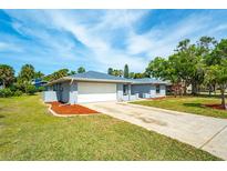 Charming single-story home featuring a two-car garage, well-maintained lawn, and tropical landscaping at 5471 Nimitz Rd, New Port Richey, FL 34652