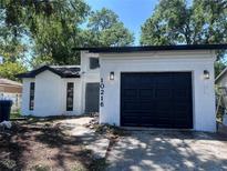Charming home featuring a black garage door, white stucco, and modern exterior lighting fixtures at 10216 N Pawnee Ave, Tampa, FL 33617
