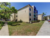 A well-maintained, light-yellow condo building featuring lush landscaping on a bright, sunny day at 14130 Rosemary Ln # 1201, Largo, FL 33774